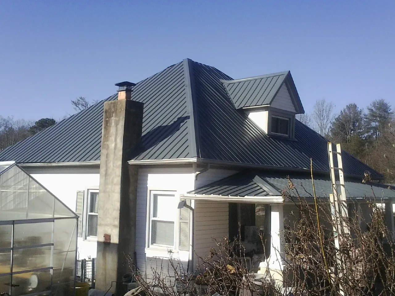 Dark blue standing seam metal roof on a white farmhouse with dormer — Slate & Tile Roof Repair by Roofing Brothers in Silver Spring