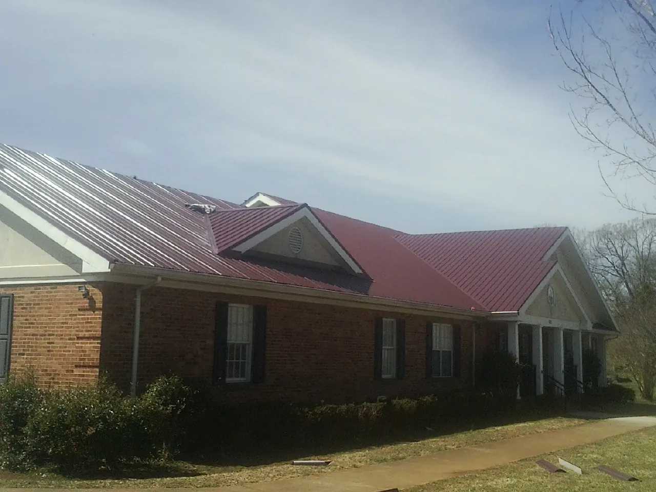 Red metal roof with gabled entries on a long brick building, from a Hail Damage Roof Repair job in Silver Spring