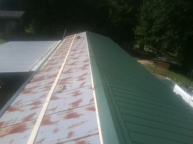 Old rusted panels beside newly installed green metal roofing — Wind Damage Roof Repair by Roofing Brothers in Silver Spring