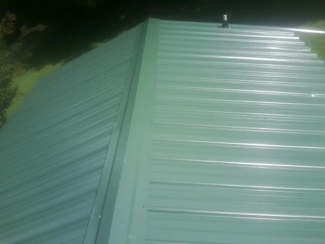 New green metal panels meeting at the ridge of a roof — Flat Roof Repair work by our crew in Silver Spring
