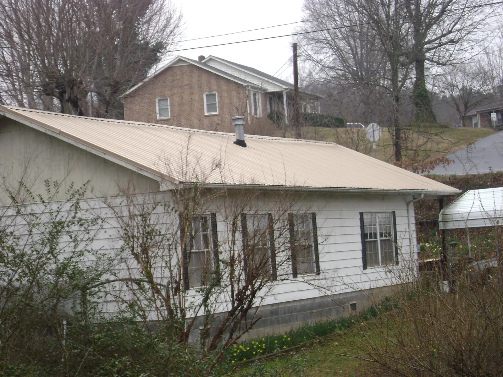 Tan metal roof on a white sided house set into a hillside — Commercial Roofing by Roofing Brothers in Silver Spring